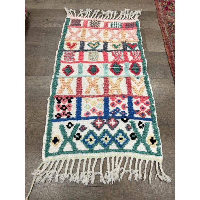 Un Tapis berbère coloré motifs multicolores | Tapis 112x64 cm avec pompons au sol, présentant des motifs multicolores.