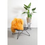 Un tapis peau de mouton jaune orange avec une plante jaune en pot.