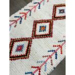 Un tapis tapis berbère écru coloré avec un motif losange, mesurant 130x68 cm.