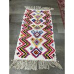 Un tapis berbère multicolore fait main avec des franges au sol. | 114x60cm