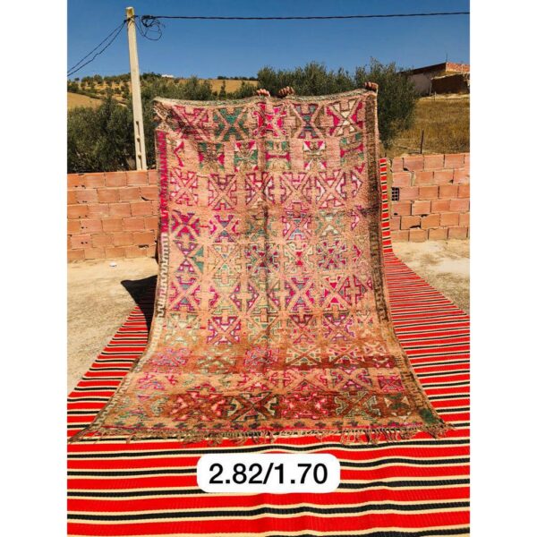 Un Tapis Boujaad coloré fait main | Tapis de 282x170 cm, sur un tapis rayé rouge et noir.