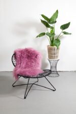 Un tapis en peau de mouton rose foncé posé sur une chaise avec une plante en pot.
