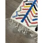 Un Tapis berbère moderne fait main fait main moderne | 121x70 cm avec franges, posé sur un parquet en bois.