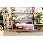 A Tapis peau de mouton islandaise rose | 100×65 cm dans une pièce avec étagères et plantes en pot.