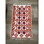 Un tapis berbère laine colorée | 115x69 cm, avec un motif rouge, orange et blanc.