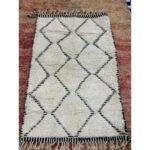 Un tapis Tapis Beni Ouarain noir et blanc, mesurant 160x104 cm, sur un Tapis Beni Ouarain beige | Tapis 160x104 cm.