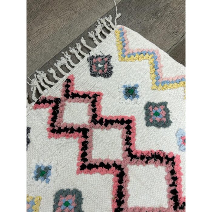 Un Tapis berbère laine fait main mesurant 108x67 cm, réalisé en laine blanche et rose avec franges et pompons.