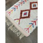 Un tapis blanc avec des franges et des pompons colorés. Ce Tapis berbère écru, 130x68 cm ajoute une touche vibrante à n'importe quel espace.