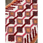 Un tapis berbère coloré en laine avec un design rose, orange et rouge.