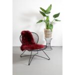 Un tapis peau de mouton rouge merlot de 100×65 cm avec un siège en peau de mouton et une plante en pot.