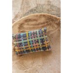 Un oreiller avec un plaid multicolore sur du sable.