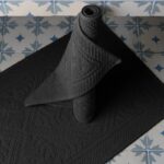 Un tapis de bain noir sur un sol carrelé.