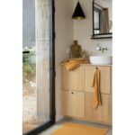 Une salle de bain avec un tapis jaune et des armoires en bois.