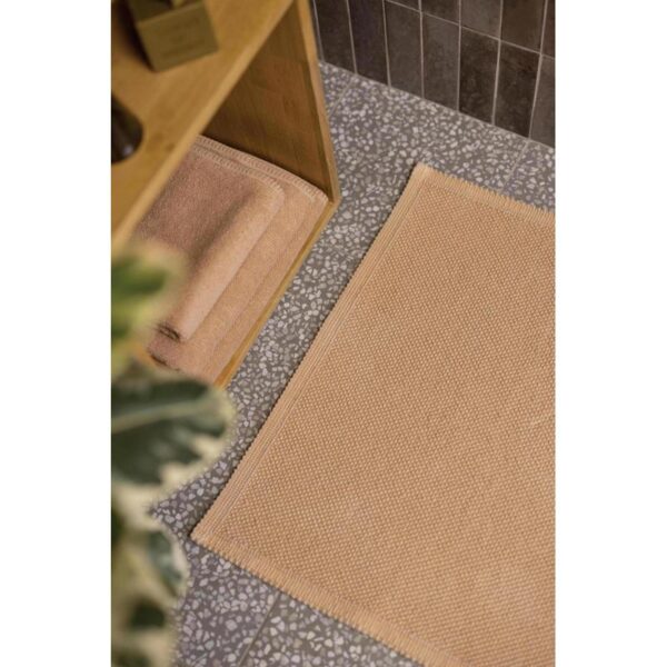 Un tapis de bain beige sur le sol.