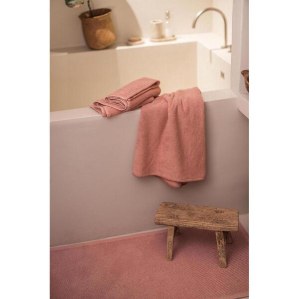 Une serviette rose est posée sur un tabouret dans une salle de bain.