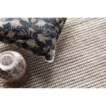 Un oiseau sur un tapis avec un vase à côté.