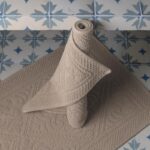 Un tapis de bain beige sur un sol carrelé.