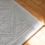 Un tapis de bain blanc sur un parquet en bois.