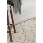 Tapis beige à motifs géométriques avec tabouret en bois.