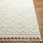 Tapis beige à motifs géométriques et pompons.