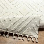 Tapis beige à motifs géométriques et franges sur parquet.