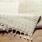 Tapis beige à franges sur plancher en bois.