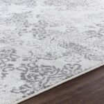 Tapis motif floral gris sur sol en bois.