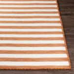 Tapis rayé orange et blanc sur plancher en bois.