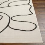 Tapis moderne beige avec motifs abstraits noirs.