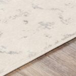 Tapis beige à motifs gris sur plancher en bois.
