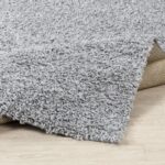Tapis moelleux gris sur plancher en bois.