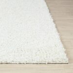 Tapis blanc shaggy sur sol en bois.