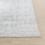 Tapis blanc motifs gris sur plancher en bois.