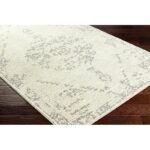 Tapis beige motif floral élégant sur parquet brun.