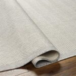 Tapis beige enroulé sur parquet brun.