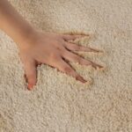 Main caressant un tapis beige texturé.