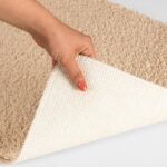 Main levant un coin de tapis beige.