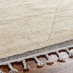 Tapis beige à franges sur parquet.