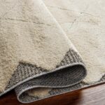 Tapis beige doux rebordé sur plancher en bois.