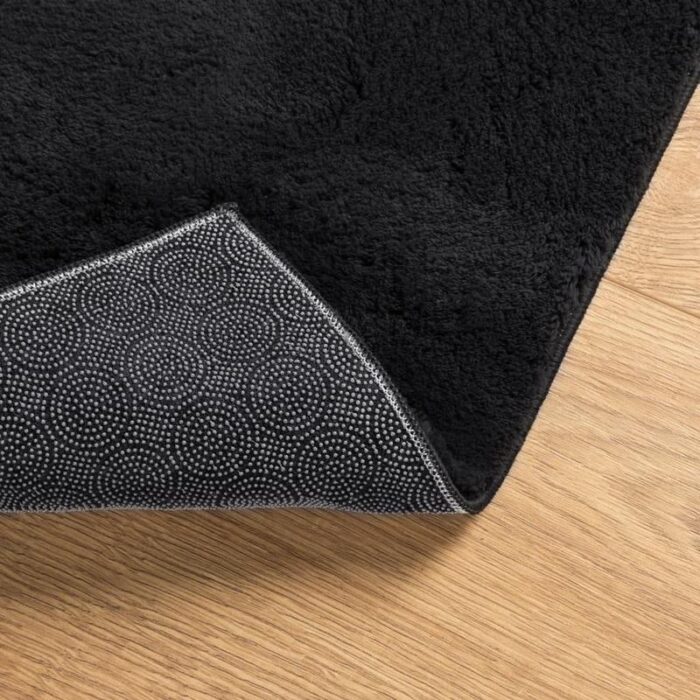 Tapis noir moelleux sur parquet avec coin relevé.